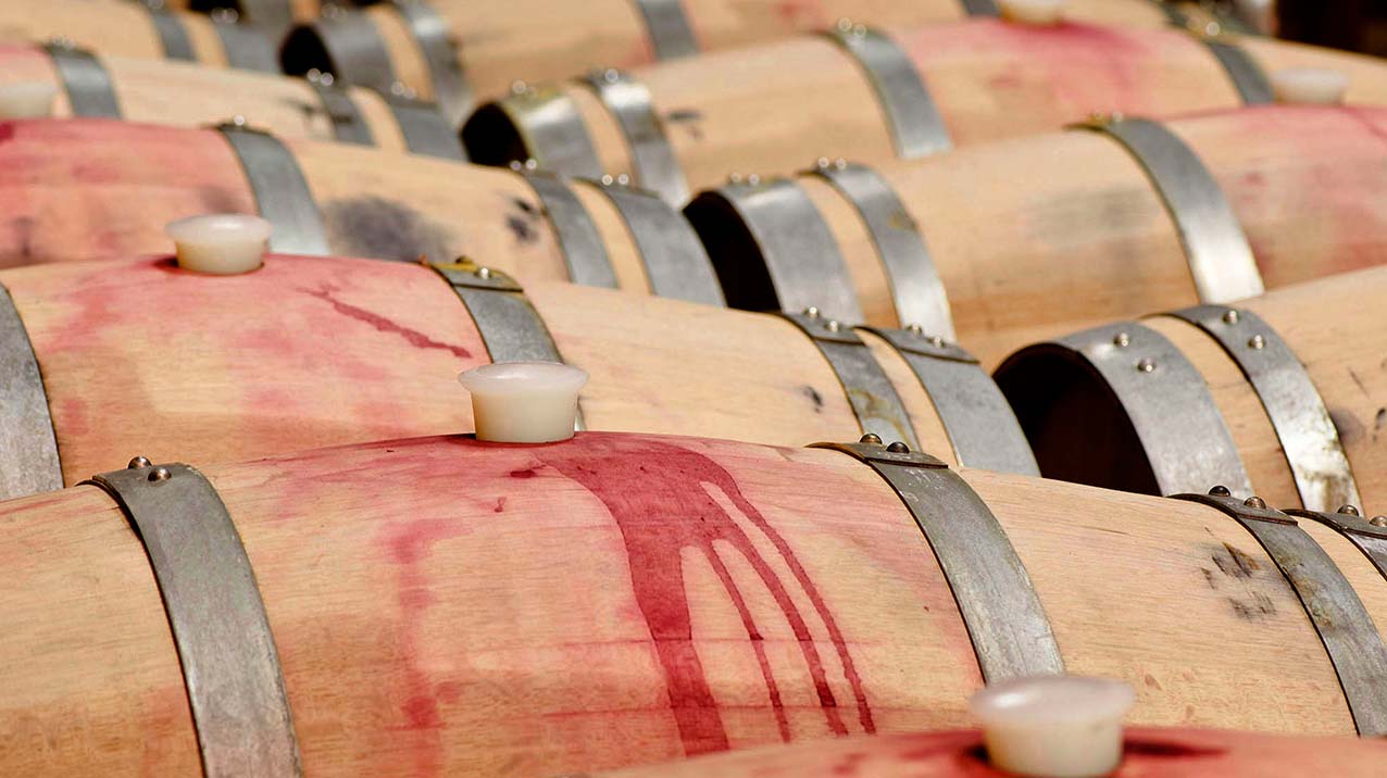 Two rows of wine barrels with red wine spilled across the wood
