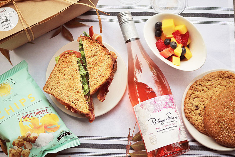 A birds eye view of a picnic spread with fruit, sandwich, cookies and a bottle of Rodney Strong Rose