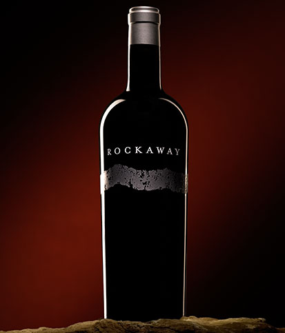 A single bottle of single vineyard Cabernet against a shadowed red background