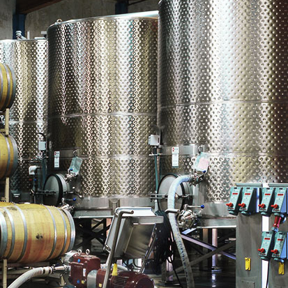 A row of tall stainless steel fermentation tanks next to winemaking equipment