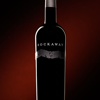 A single bottle of single vineyard Cabernet against a shadowed red background